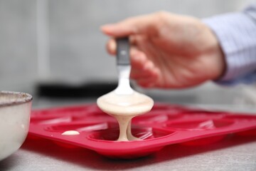 Woman pouring batter into baking mold at table, closeup. Madeleine cookies
