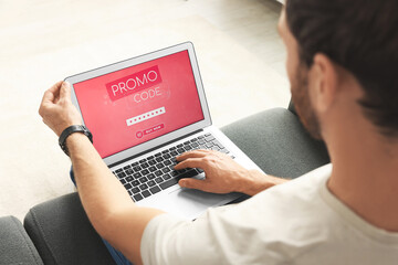 Man holding laptop with activated promo code on sofa, closeup