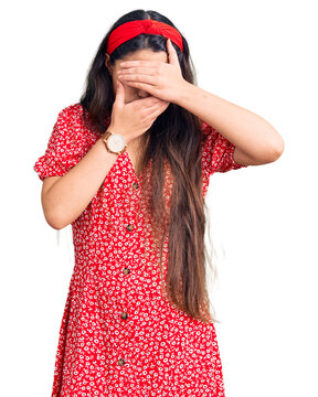 Brunette teenager girl wearing summer dress covering eyes and mouth with hands, surprised and shocked. hiding emotion