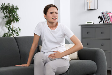 Young woman suffering from cystitis on sofa at home - obrazy, fototapety, plakaty