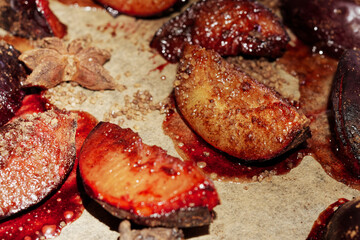 Baked plum wedges with cinnamon, sugar and star anise on a baking sheet