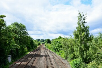 Railways running parallel to each other, surrounded by lush greenery under a bright cloudy sky