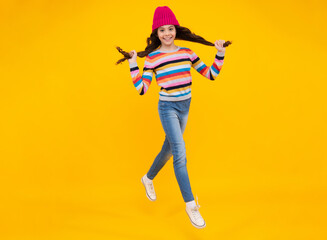 Fototapeta na wymiar Beautiful teen girl in a winter hat and a warm sweater. Jump and run. A child on a yellow isolated background. Happy teenager, positive and smiling emotions of teen girl.