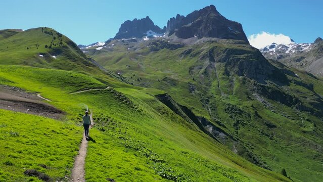 Young Adult Woman hikes green valley to mountains in French Alps - Aerial Follow