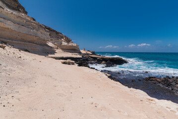 Fototapeta na wymiar Dark beach with steep white rocky desert cliff and untamed Atlantic ocean, Fuerteventura 
