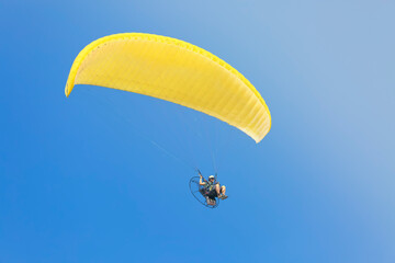 A yellow paraglider with a paramotor, soaring in the rays of the evening sun.