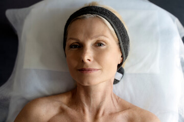 Mature woman laying at the couch and smiling while making beauty procedures top view