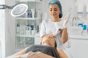 Charming young beautician in white lab coat taking on protective gloves