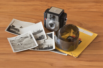 1960s plastic snapshot camera with roll of 127 size film negatives and black and white prints on a wooden table top