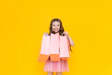 A child holds paper bags with purchases after shopping. Sale and shopping for little girls. A charming girl holds gift bags on a yellow isolated background.