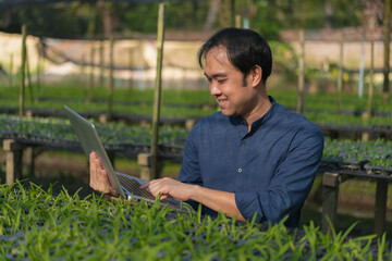 Young man farmer working at his orchid farm. Young man notes the information on the notepad to track the growth of orchid. Portrait asian small business owner of orchid gardening farm. 