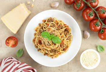 Spaghetti bolognese with fresh basil, tomatoes, garlic and parmesan cheese on a beige background. Pasta with beef stew sauce in a white plate, top view. Traditional Italian food.
