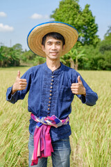 Asian male farmer wearing traditional blue dress standing with thumbs up two hands There was a smiling face at the farm.