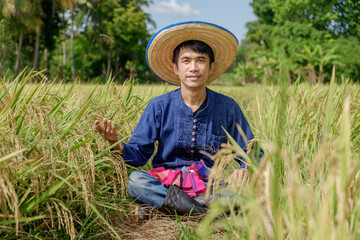 Naklejka na ściany i meble Asian male farmer wearing traditional blue dress Sitting raising his hands with a smiling face in the middle of the field