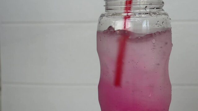 Use a plastic straw to mix soda and red water in a bottle.