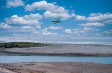 Fototapeta na wymiar A bridge on the sea shore, airplane flying in the sky, sun setting.
