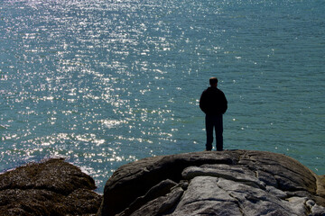 man on the rock cliff looking at the water