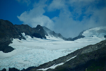 glacier in a valley of a mountain in Alaska with blue skies and white clouds