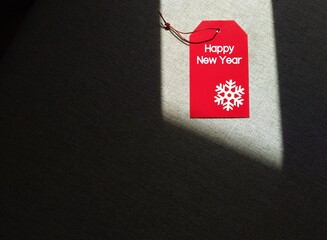 Red gift tag with text HAPPY NEW YEAR on copy space dark shadow background, concept of new year...