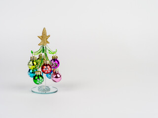 New Year's Eve photo with a glass Christmas tree, decorated with toys, standing on a white background. There is room for text.