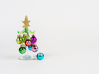 New Year's Eve photo with a glass Christmas tree, decorated with toys, standing on a white background. There is room for text.
