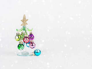 New Year's Eve photo with a glass Christmas tree decorated with toys, standing on a white background with bokeh. There is room for text.