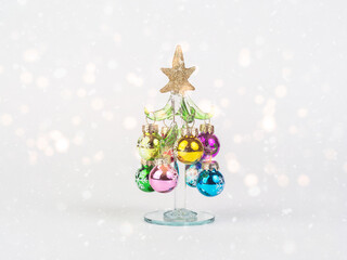 New Year's Eve photo with a glass Christmas tree decorated with toys, standing on a white background with bokeh. There is room for text.