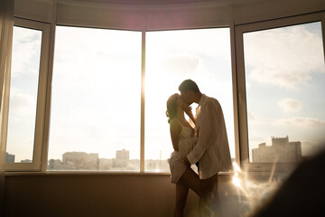 Woman and man hugging and kissing by the panoramic window at hotel. Festive morning, engagement...