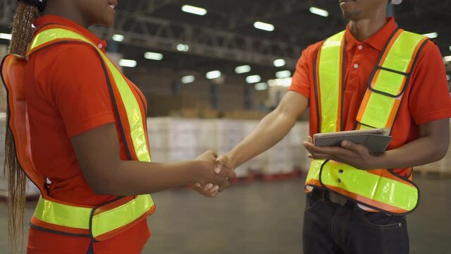 Team of a couple of black worker shaking hands in large warehouse retail store industry. Rack of stock storage. Interior of cargo in ecommerce and logistic. Depot. People lifestyle. Shipment service.