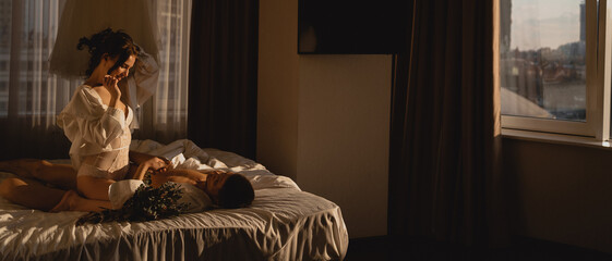 Romantic beautiful couple in love in bedroom. Young guy and girl in shirt laying in bed touching each other. Passionate night together. Banner.