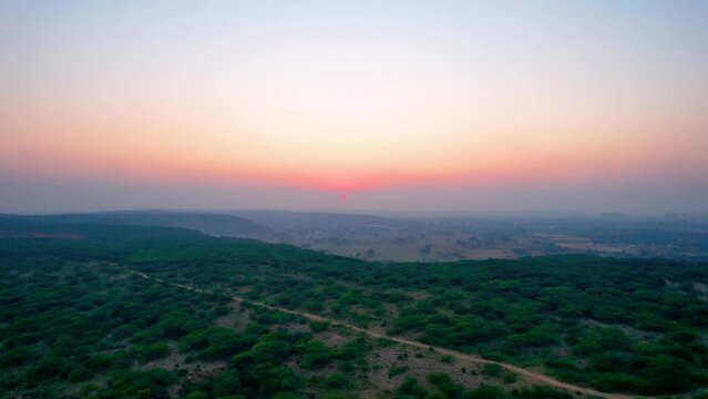 aerial drone shot gaining height showing sunset dusk colors over tree covered mountain top with small dust trail and fog covered mountains in the distance shot at leopard trail gurgaon haryana popular
