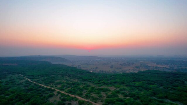 aerial drone shot showing sunset dusk colors over tree covered mountain top with small dust trail and fog covered mountains in the distance shot at leopard trail gurgaon haryana popular local tourist