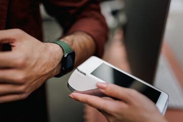Female holding a payment machine while businessman paying with a smart watch.
