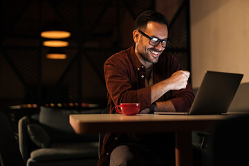Obraz na płótnie Canvas Smiling man having an online meeting, working late at night.