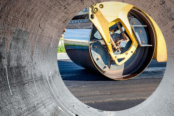 Vibratory road roller lays asphalt on a new road under construction. Close-up of the work of road construction equipment. Modern work on the construction of city streets. View from the big pipe.