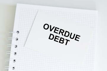 a white card with overdue debt text on the background of a white notebook on the table, business...