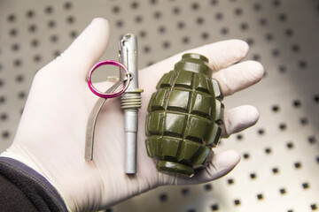A disassembled grenade lies on a hand in a rubber glove
