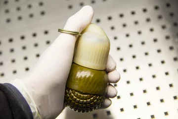Rolgordijnen Male hand in a rubber glove holds a grenade close-up © aleksmark2016