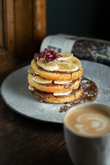 Vertical shot of delicious pancakes with chocolate and banana and a cup of cappuccino