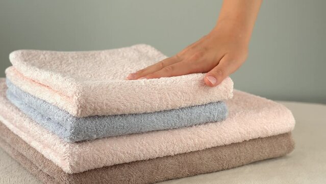 Female hands touches stacked cotton terry towels. Bathing, washing, and cleanliness concept. Washing powder, fabric softener. Household, hotel, spa.
