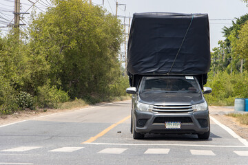 A pick-up with a big load covered the black tarpaulin drives to the rural road, Thailand