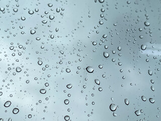 View of glass with water drops, closeup. Raindrops on the window.  View through the window when raining. Rain drops on window glasses surface with cloudy background.