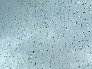 View of glass with water drops, closeup. Raindrops on the window.  View through the window when raining. Rain drops on window glasses surface with cloudy background.