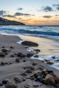 Stunning landscape image of Sennen Cove in Cornwall during sunset with dramatic sky and long exposure sea motion