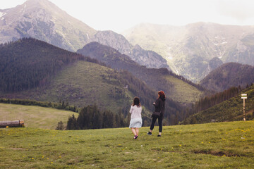 Two young girls walking on a green meadow among the mountains