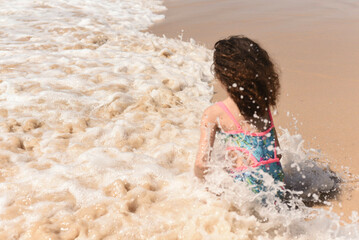 Fototapeta premium Child playing at the water's edge on the beach and with flowing hair