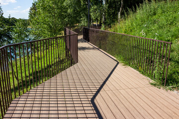 Walking footbridge with a railing laid along the coastal slope near the reservoir