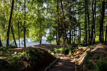 Fototapeta premium Descent from the slope to the observation deck on the shore of the reservoir. Pond on the river Stradalovka: Balabanovo, Russia - August 2022