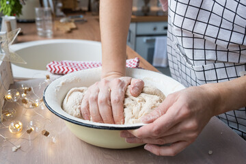 Hands knead thick dough on the kitchen table, decorated with festive decorations for Christmas and New year. Baking at home, aroma and comfort. Close-up