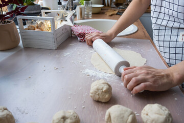 Hands knead thick dough, roll out with a rolling pin on the kitchen table, decorated with festive...